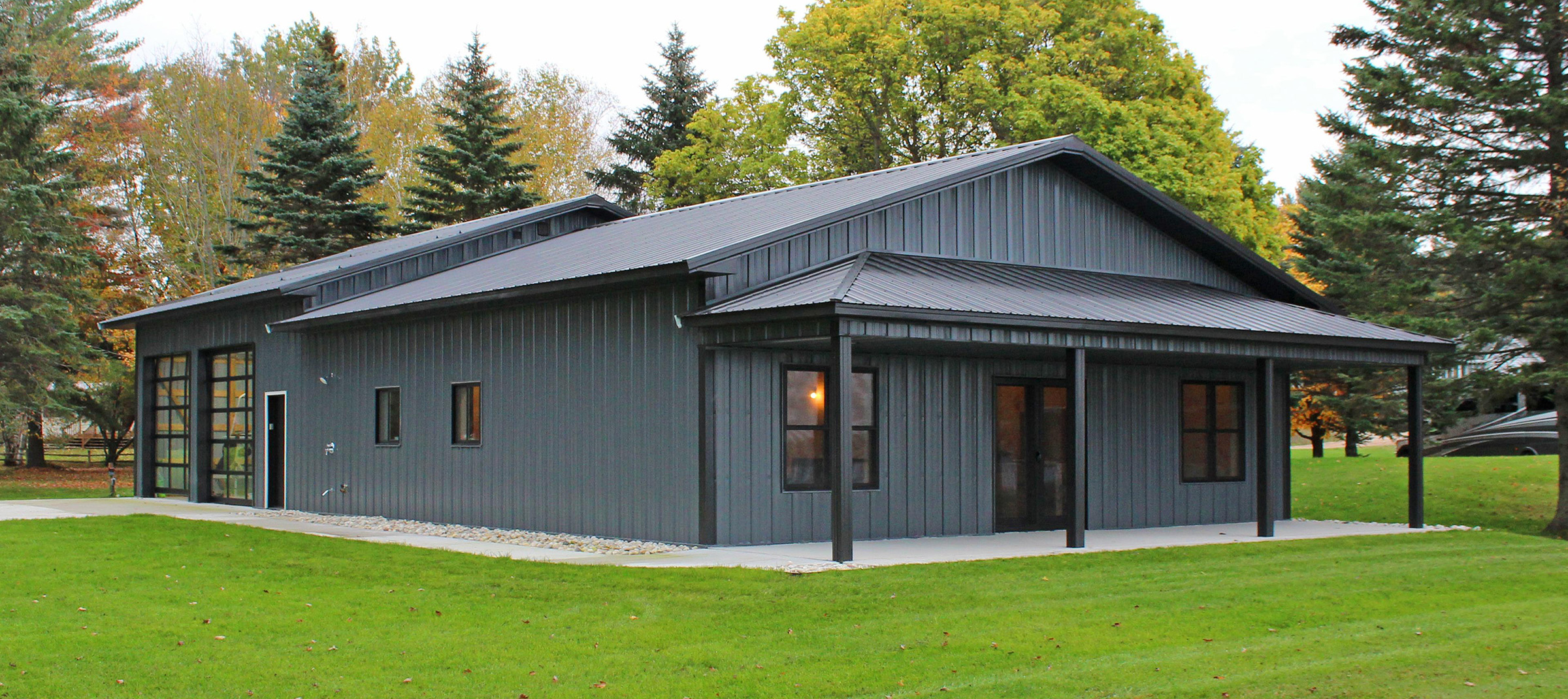 Gray postframe suburban building featuring dark gray trim, an overhang and garage