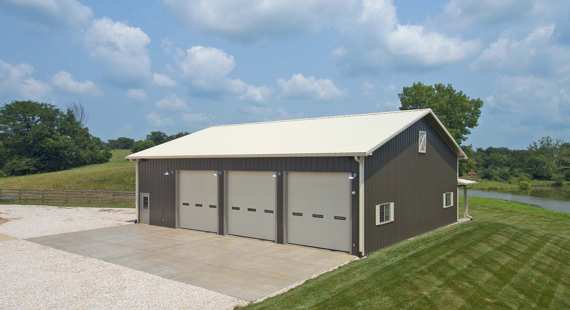 gray suburban postframe building featuring three pulldown doors and a white roof sitting on a body of water